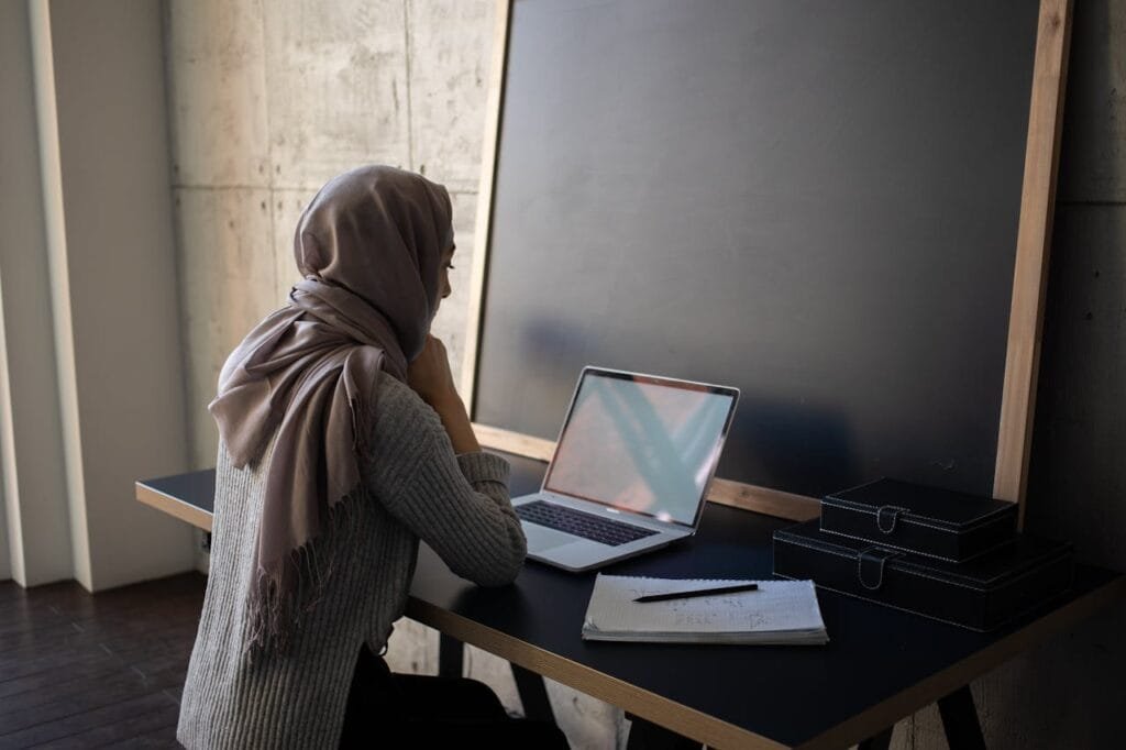 pexels-photo-6281990 Side view of Muslim female student in traditional headscarf looking at screen of netbook while preparing for lesson an table with workbook near blackboard