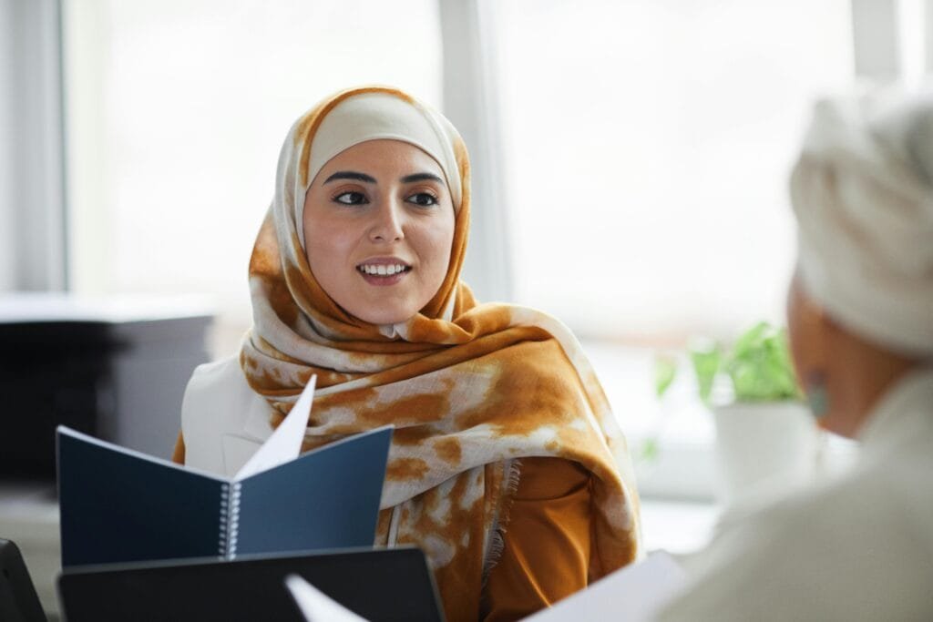 A young woman wearing a hijab is engaged in a professional discussion indoors.