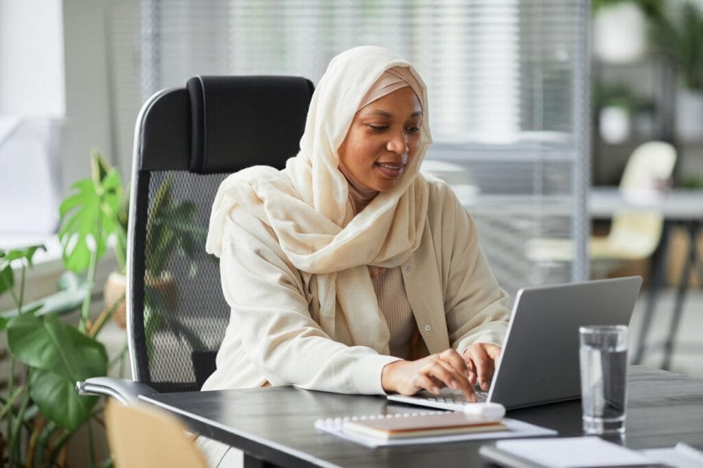 pexels-photo-8154765 Professional Muslim businesswoman in hijab working on laptop in a modern office setting.