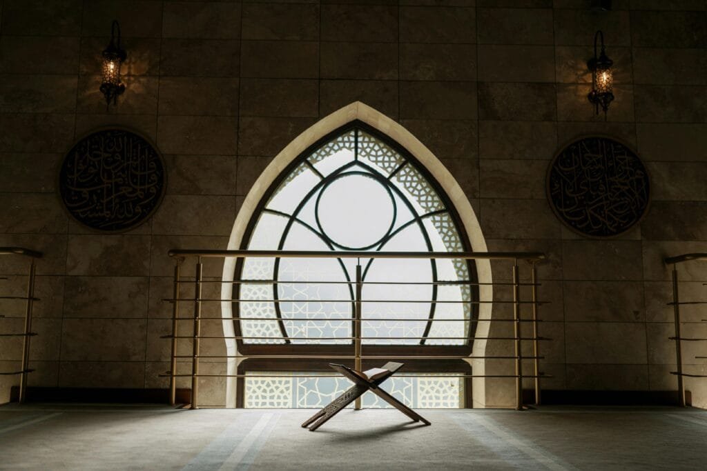 pexels-photo-8164749-8164749 A peaceful mosque interior featuring a backlit window, rehal stand, and intricate architecture.